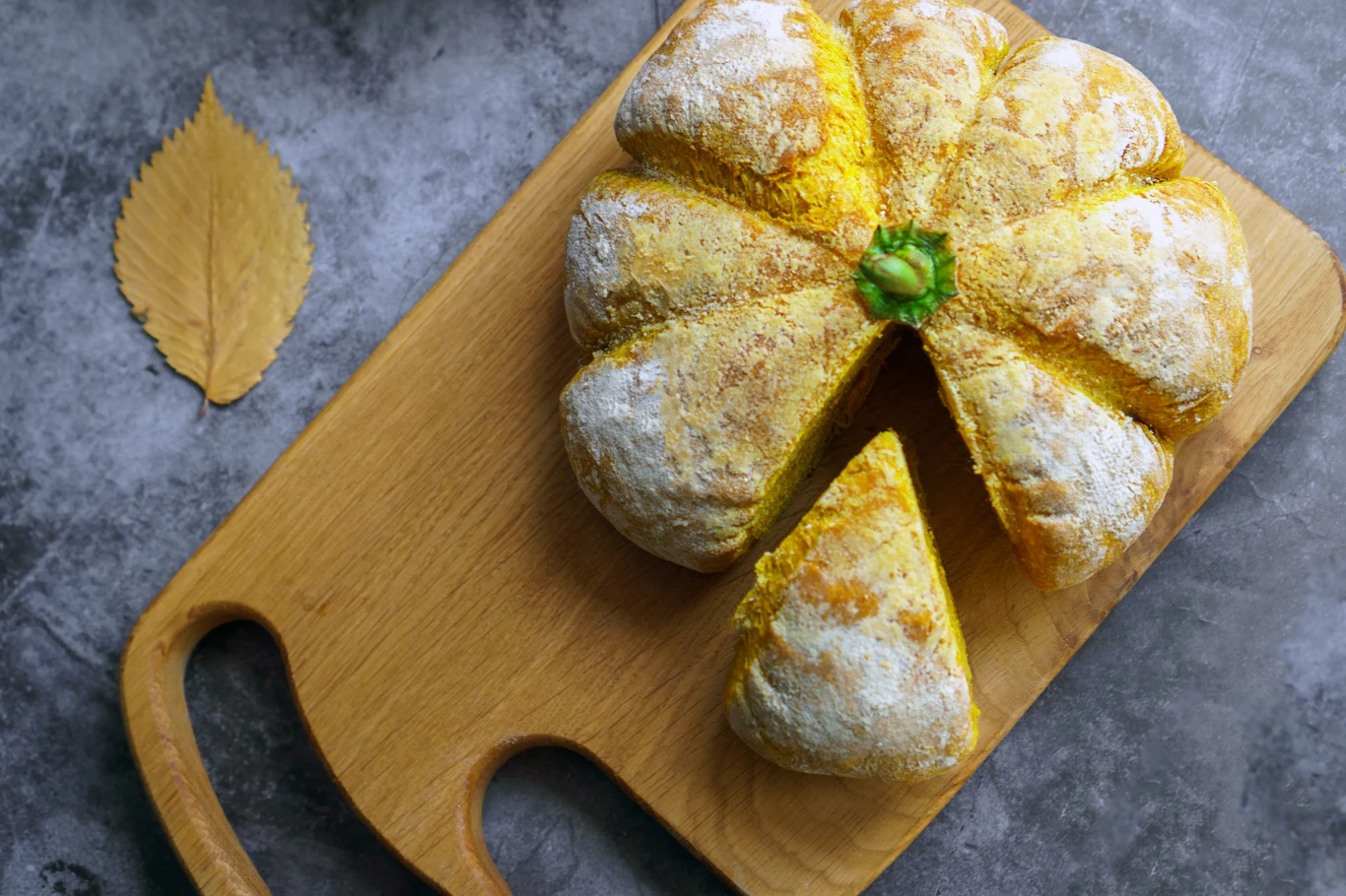 Chleb kukurydziany to pyszna propozycja na jesień. Poznaj prosty przepis na cornbread. Chleb w kształcie dyni z wyraźnie oddzielonym jednym kawałkiem, ułożony na drewnianej desce do krojenia. Cornbread.