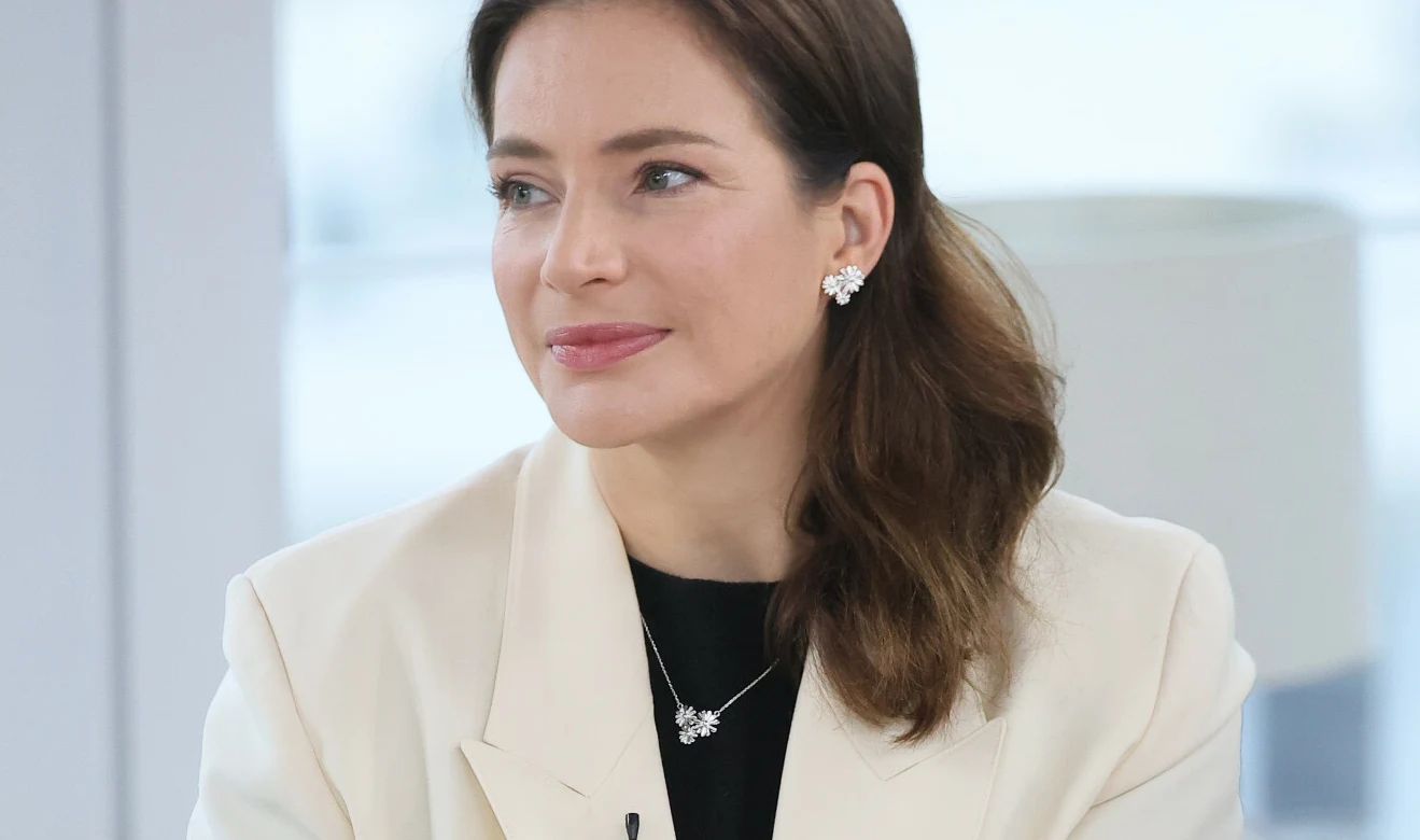 Anna Dereszowka Anna Dereszowska w kremowej marynarce i srebrnej biżuterii siedząca w jasnym wnętrzu.