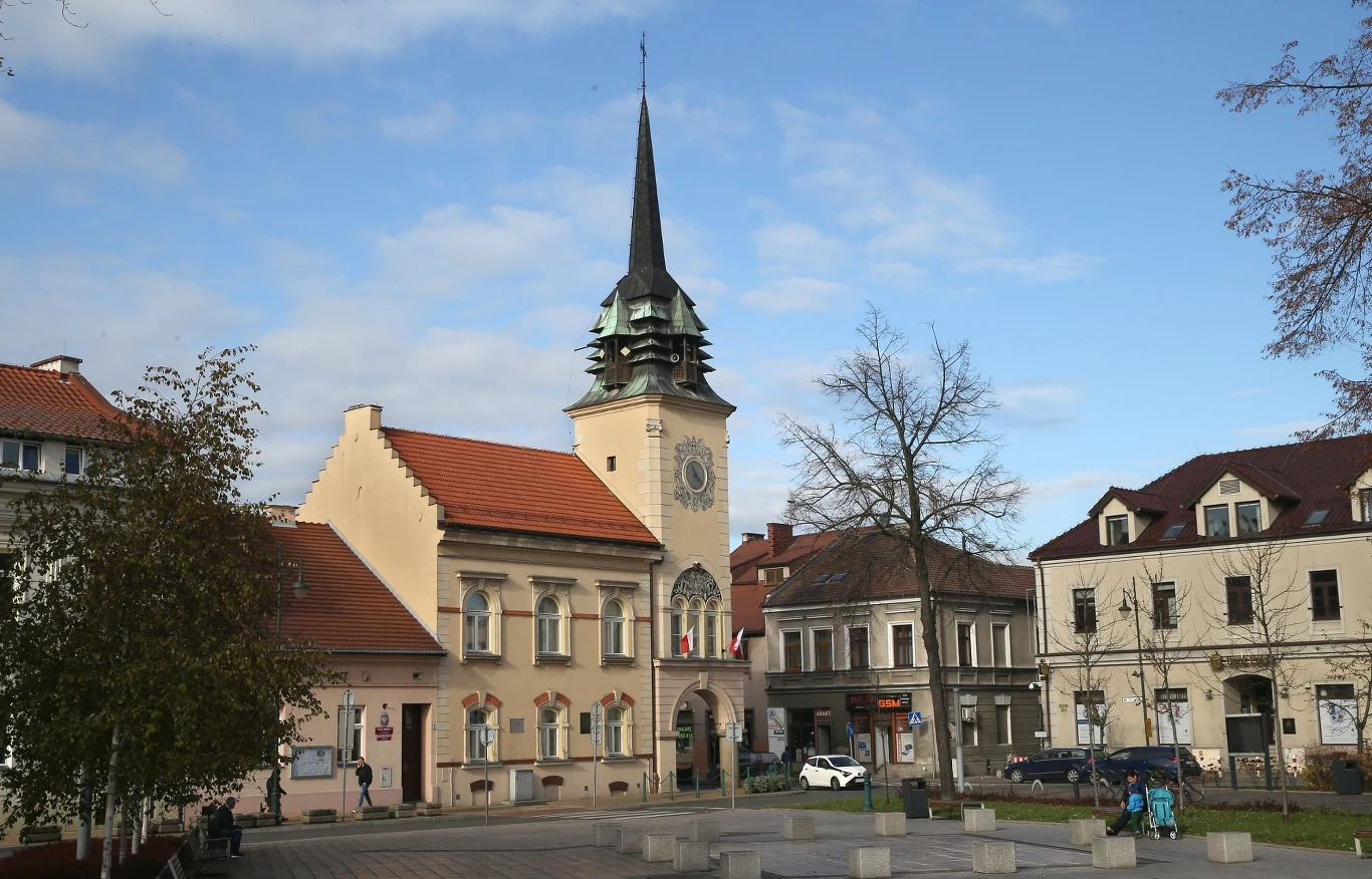 Jak zmieni się strefa płatnego parkowania w Skawinie? Radni pracują nad nową uchwałą. Zabytkowy ratusz w Skawinie z wieżą zegarową, otoczony kamienicami i miejskim placem z drzewami i ławkami.