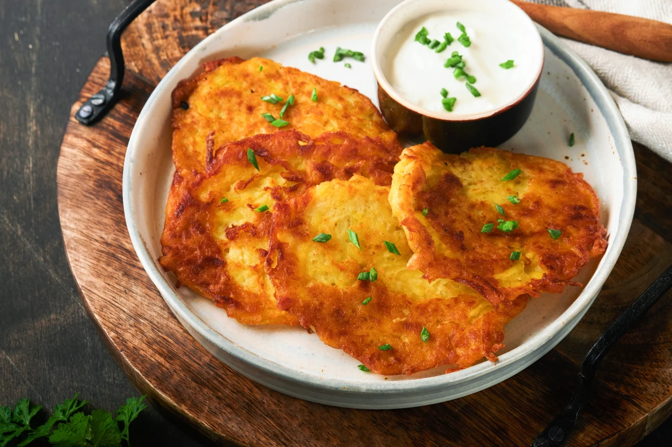 Placki ziemniaczane z parmezanem. Są wyraziste w smaku i niezwykle chrupiące. Placki ziemniaczane z parmezanem podane na białym talerzu z sosem czosnkowym.