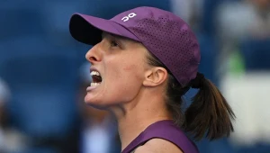 Zdenerwowana tenisistka w fioletowej czapce i stroju sportowym z otwartymi ustami, na tle rozmytej trybuny.