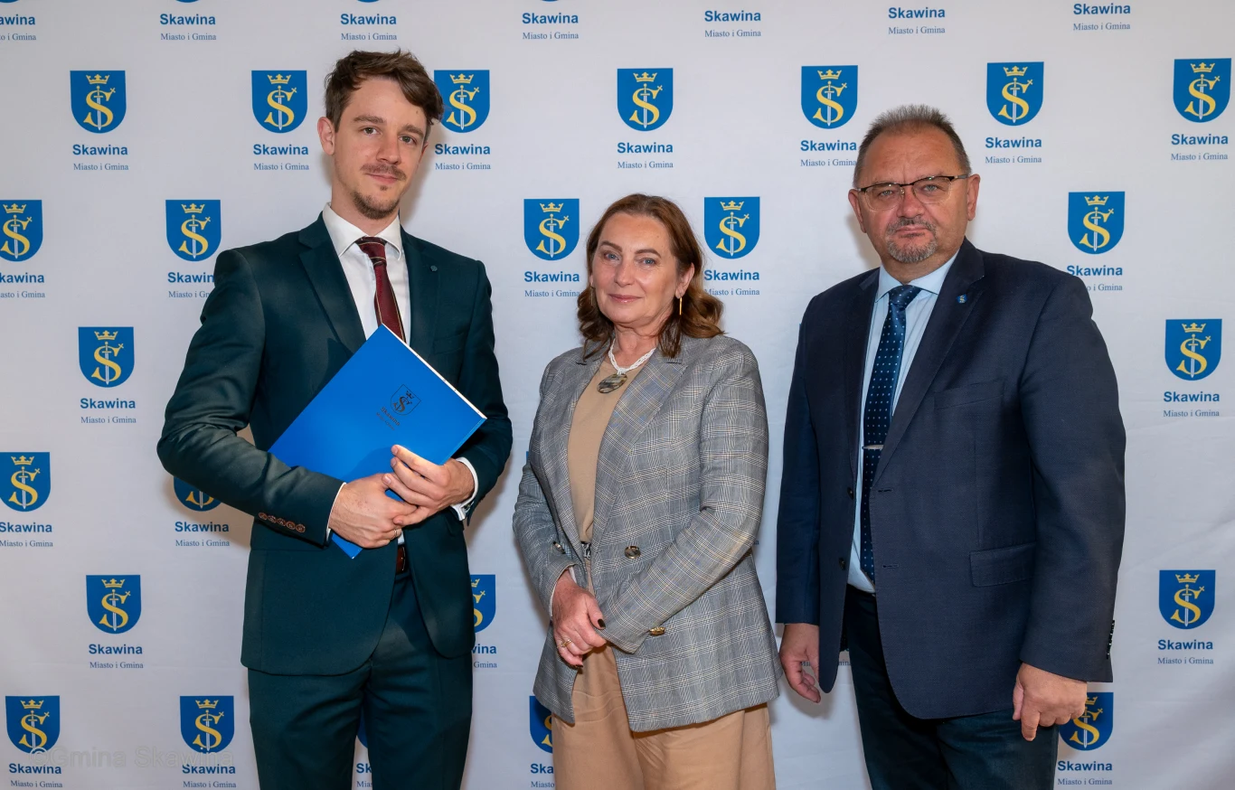 Burmistrz Skawiny Norbert Rzepisko przekazał oficjalne powołanie na stanowisko szefa Muzeum Regionalnego Rafałowi Sowie, który zastąpił Jadwigę Pierzchałę Burmistrz Skawiny wręcza Rafałowi Sowie powołanie na dyrektora Muzeum Regionalnego; trzy osoby na tle herbu miasta.