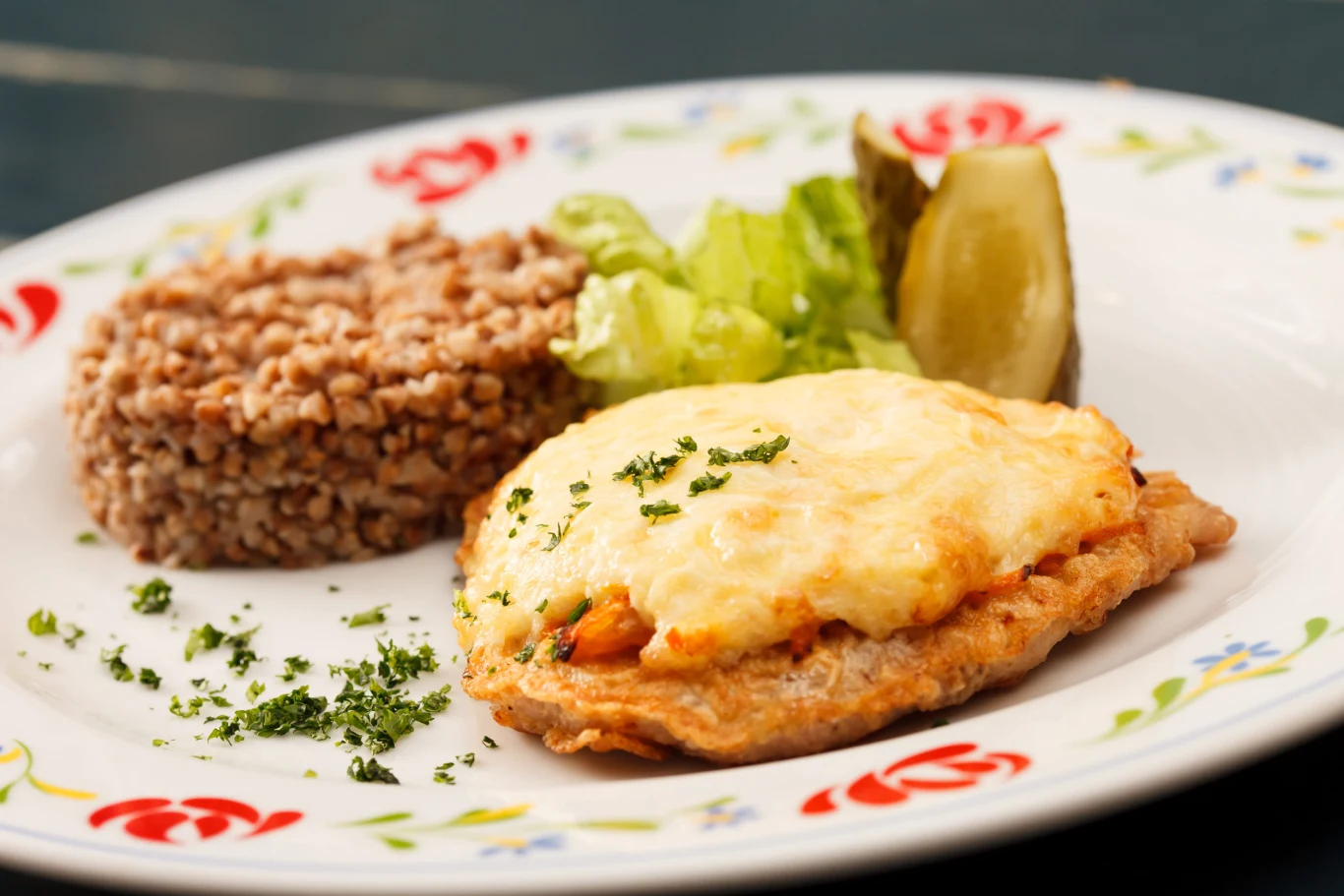 Takie kotlety robię, gdy nie chce mi się smażyć schabowych Kotlet schabowy z serem i ziołami, kasza gryczana, surówka z sałaty i ogórek kiszony na talerzu.