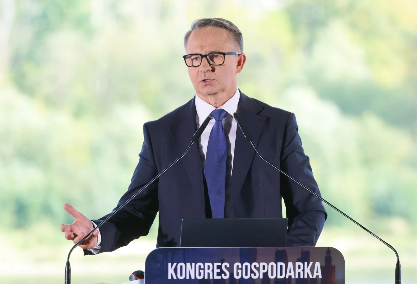 Prof. Mariusz Andrzejewski nazywany jest w PiS-ie "nowym Morawieckim". Ma być jedną z nowych twarzy partii Mężczyzna w garniturze i okularach przemawia przy mównicy z napisem 'KONGRES GOSPODARKA', gestykulując ręką.