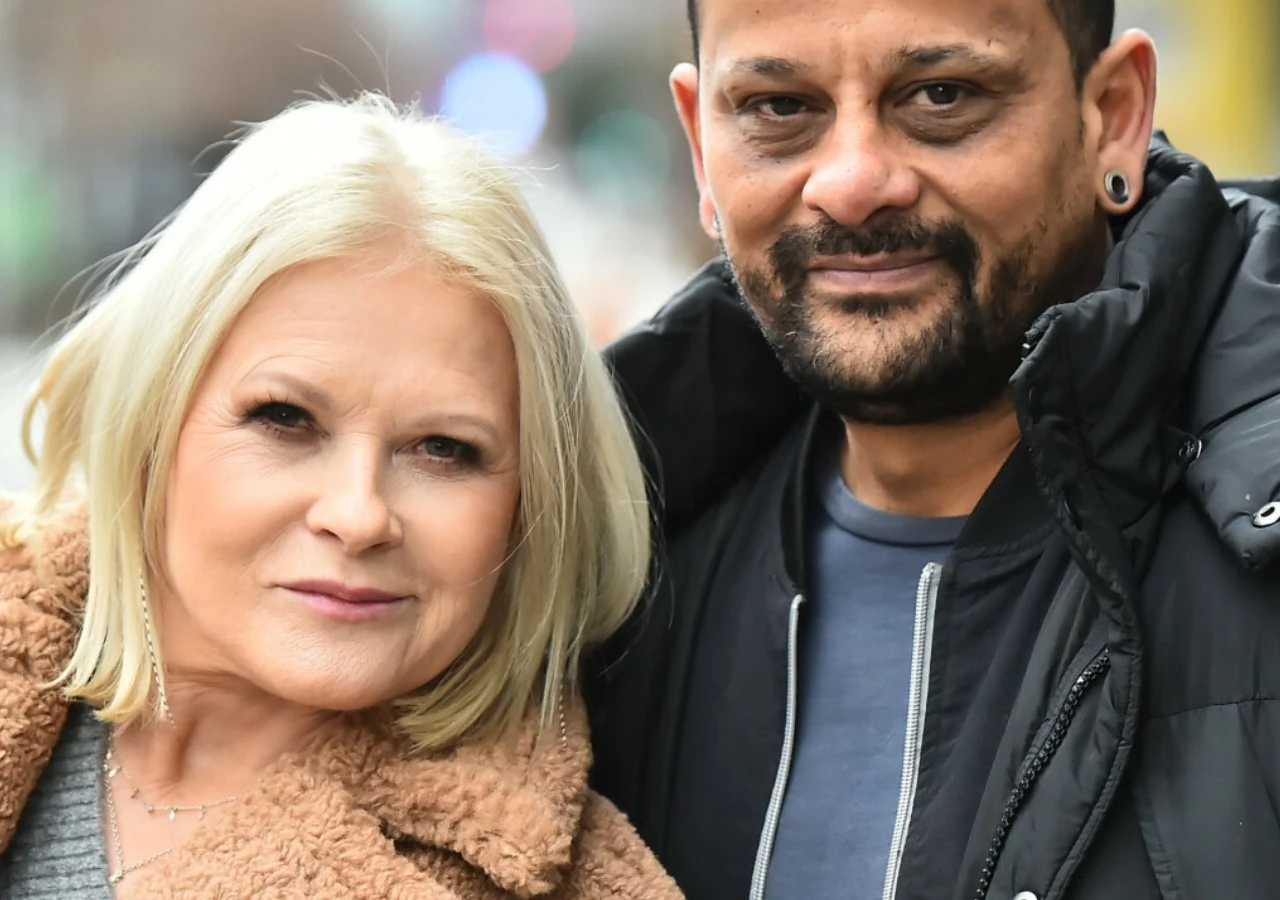 Urszula, Tomasz Kujawski Dwie osoby stoją blisko siebie, kobieta o blond włosach w brązowym płaszczu oraz mężczyzna z krótkimi ciemnymi włosami i zarostem, ubrany w czarną kurtkę.