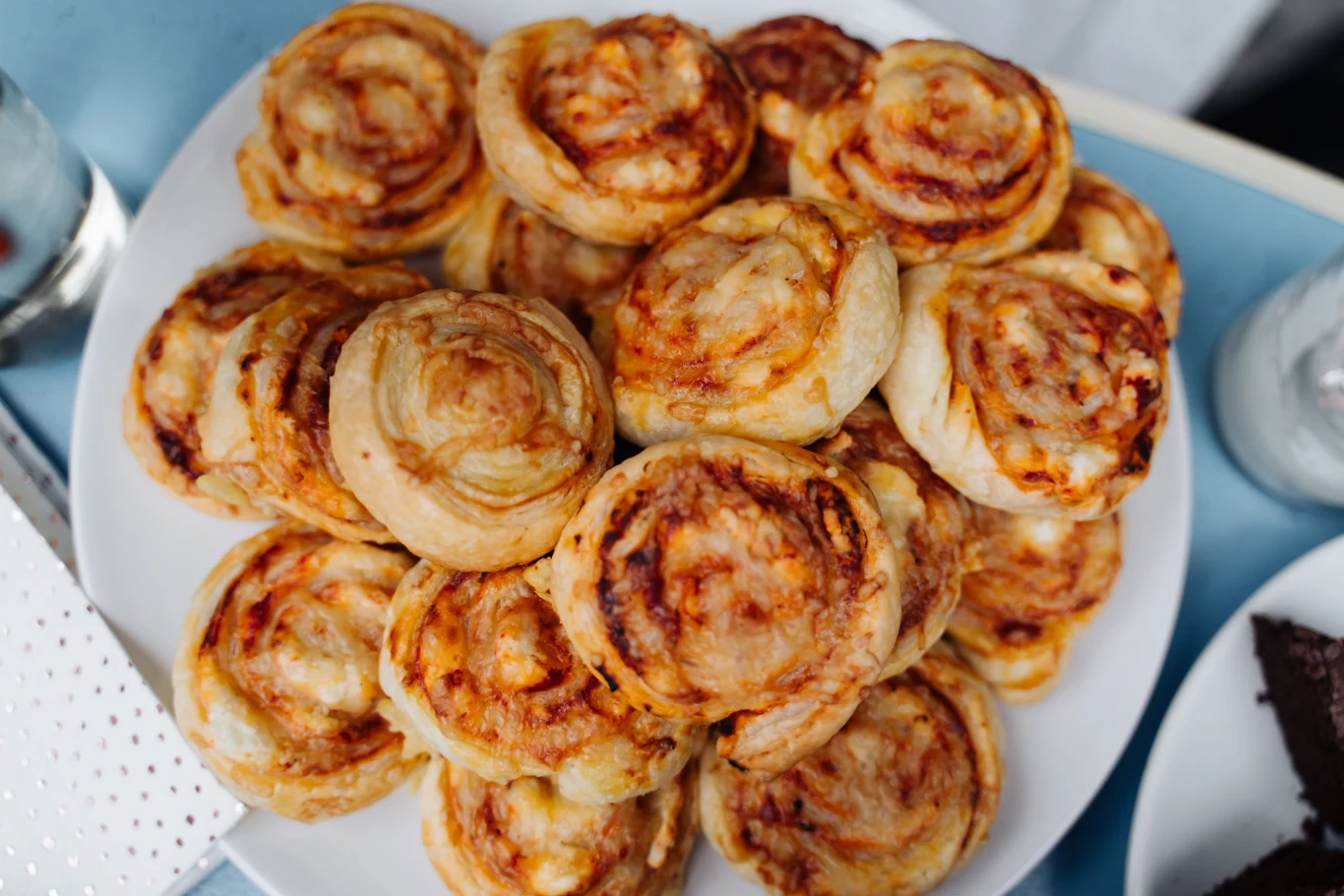 Pizzerinki z ciasta francuskiego to szybka przekąska na rodzinne imprezy Pizzerinki z ciasta francuskiego z sosem pomidorowym i serem na białym talerzu