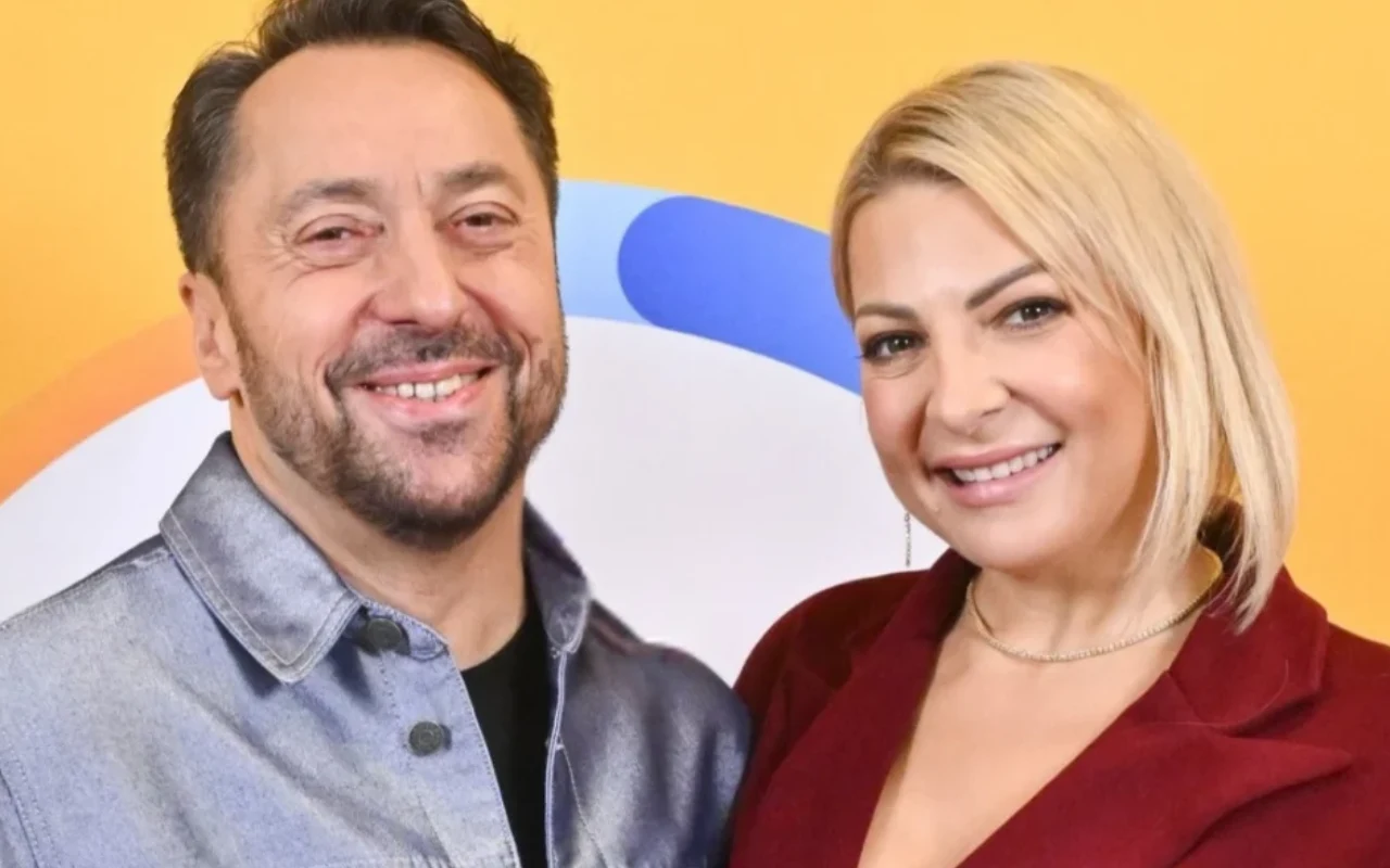 Magda Narożna-Romaniuk i Marcin Miller w "halo tu polsat" Uśmiechnięty mężczyzna w koszuli jeansowej oraz kobieta w bordowej marynarce pozują razem na tle w jasnych kolorach.