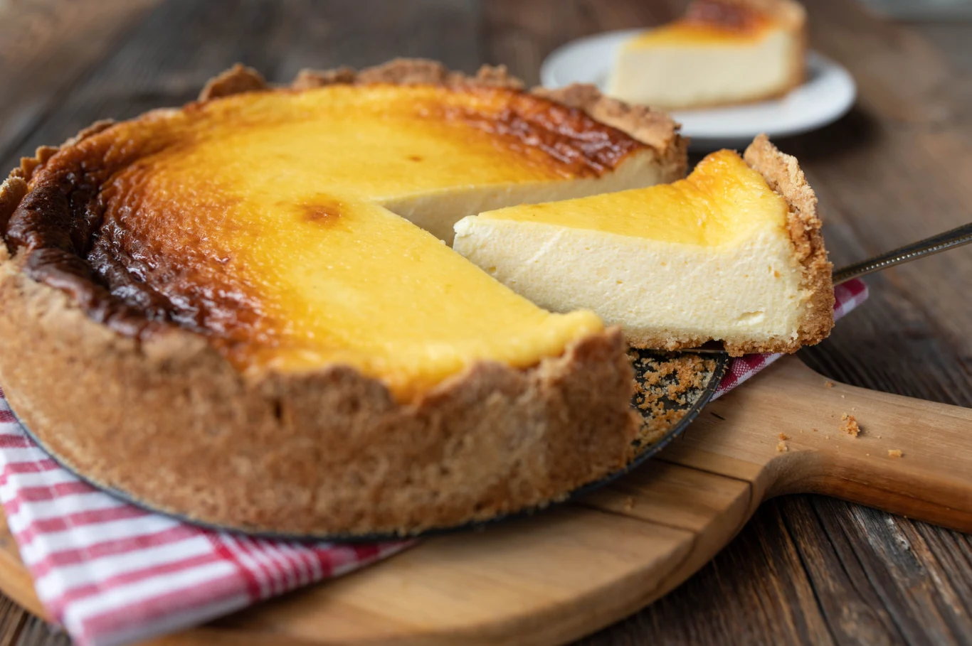 Käsekuchen - niemiecki sernik, różni się nieco od polskiego. Käsekuchen, niemiecki sernik, ukrojony kawałek na łopatce, na drewnianej desce z ściereczką.