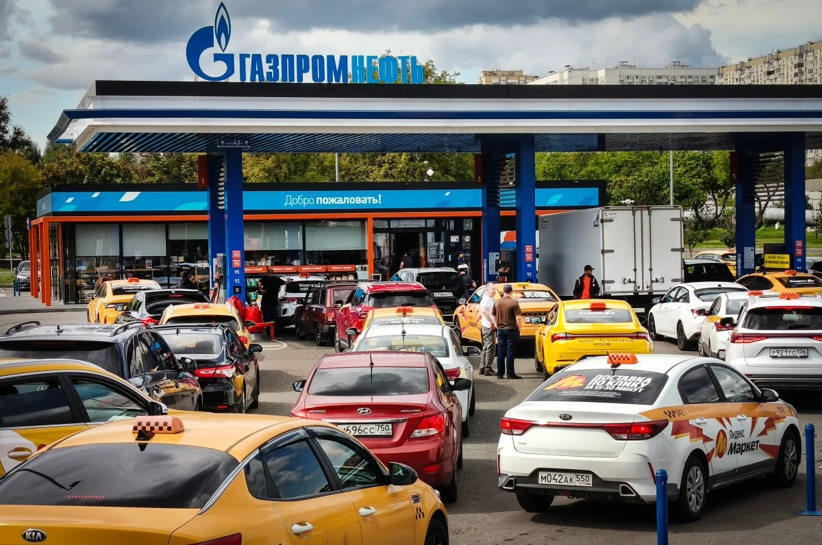 Stacja paliw Gazprom z dużą liczbą samochodów, w tym wiele oznaczonych jako taksówki, oczekujących w długiej kolejce do dystrybutorów.