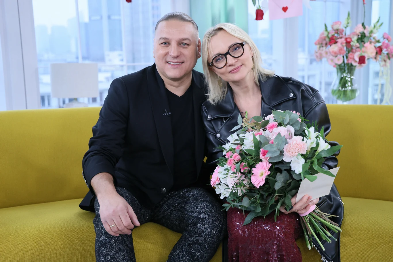 Łukasz i Edyta Golcowie Edyta Golec i Łukasz Golec siedzący na żółtej sofie. Edyta Golec trzyma bukiet różowych i białych kwiatów.