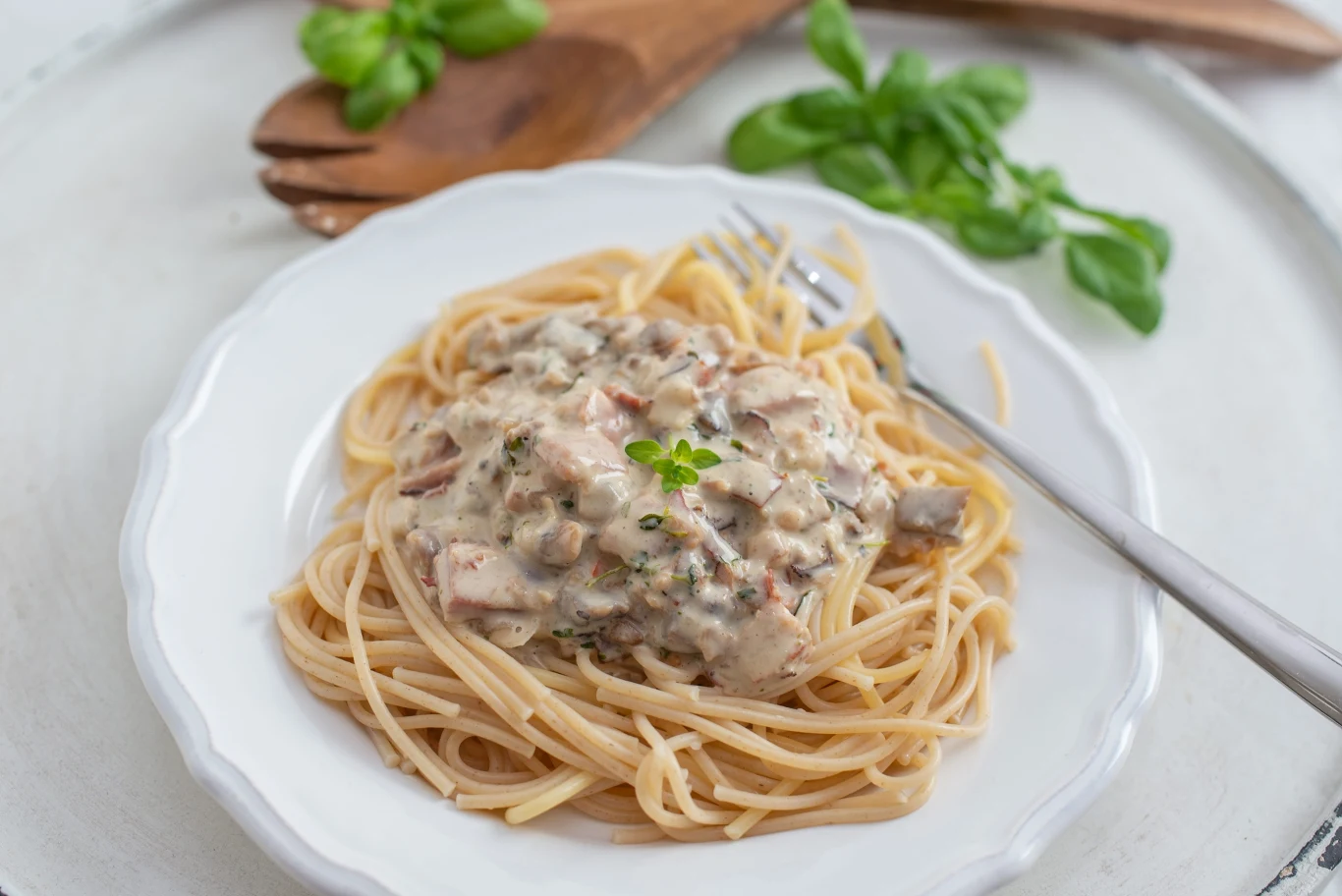 Spaghetti w najlepszym, kremowym sosie z czosnkiem i parmezanem. Szybki obiad godny włoskiego mistrza spaghetti z kremowym sosem śmietanowym, kawałkami grzybów i ziół, udekorowane bazylią na białym talerzu