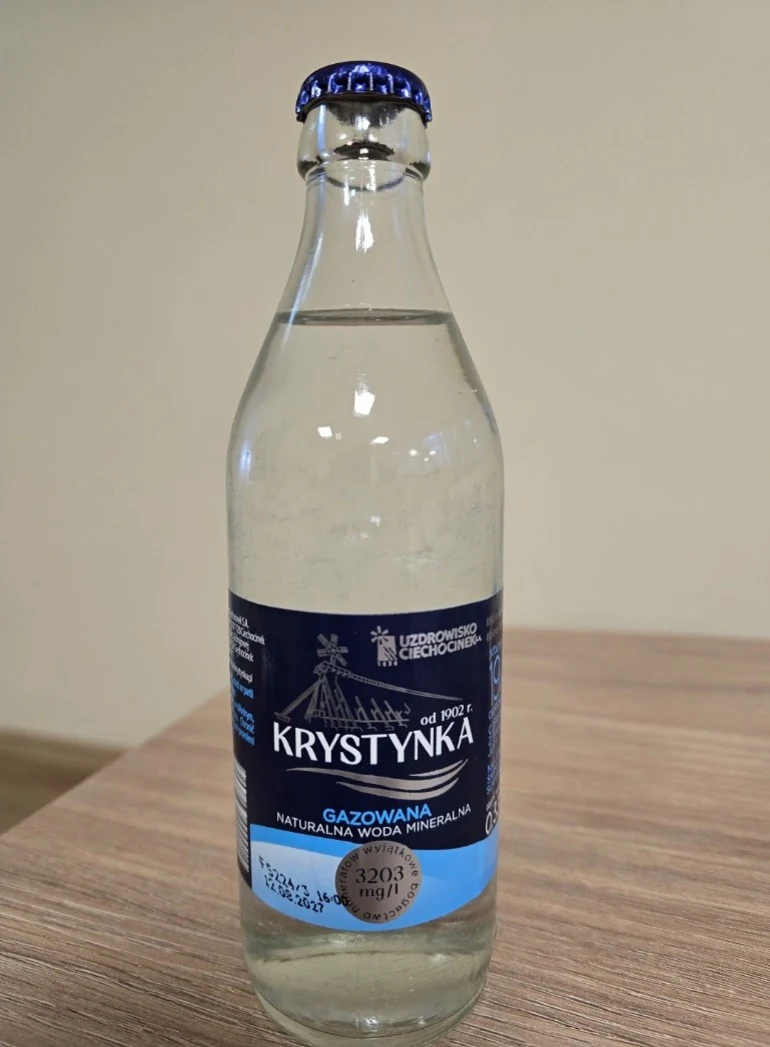 butelka gazowanej naturalnej wody mineralnej marki Krystynka stojąca na drewnianym blacie