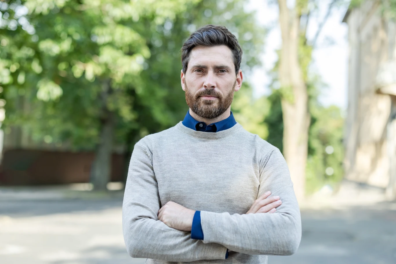Aleksander to imię kojarzone z siłą Mężczyzna z brodą w szarym swetrze stoi z założonymi rękami na tle zielonych drzew i zabudowań