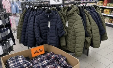 Oliwkowe i granatowe kurtki pikowane na wieszaku w dziale z odzieżą w dyskoncie, dłoń klientki wysuwa jedną z nich