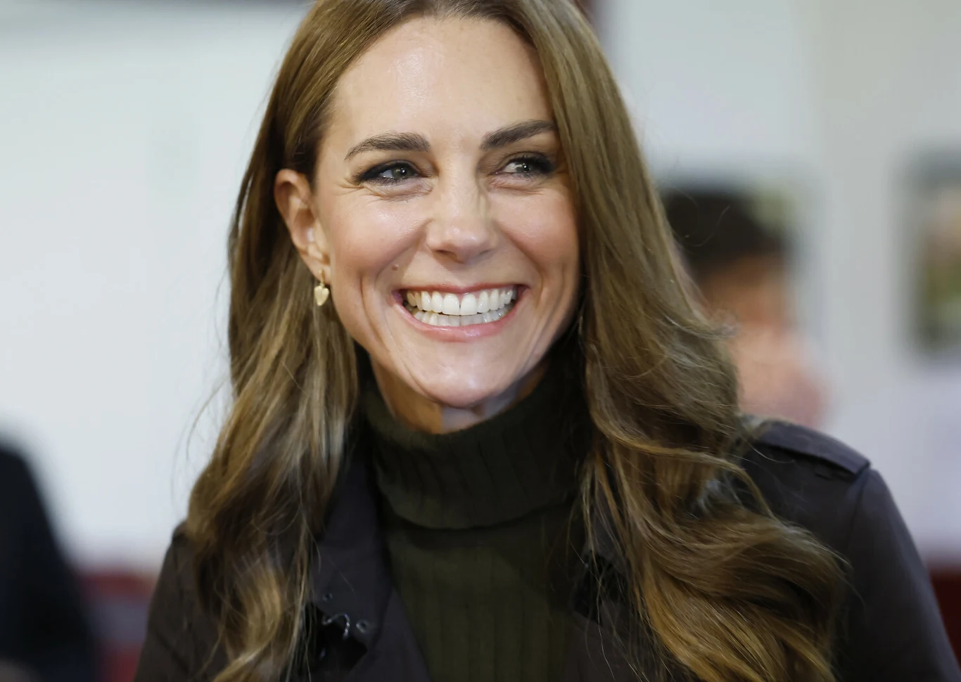 Księżna Kate Księżna Kate z uśmiechem, ubrana w ciemny golf i marynarkę.