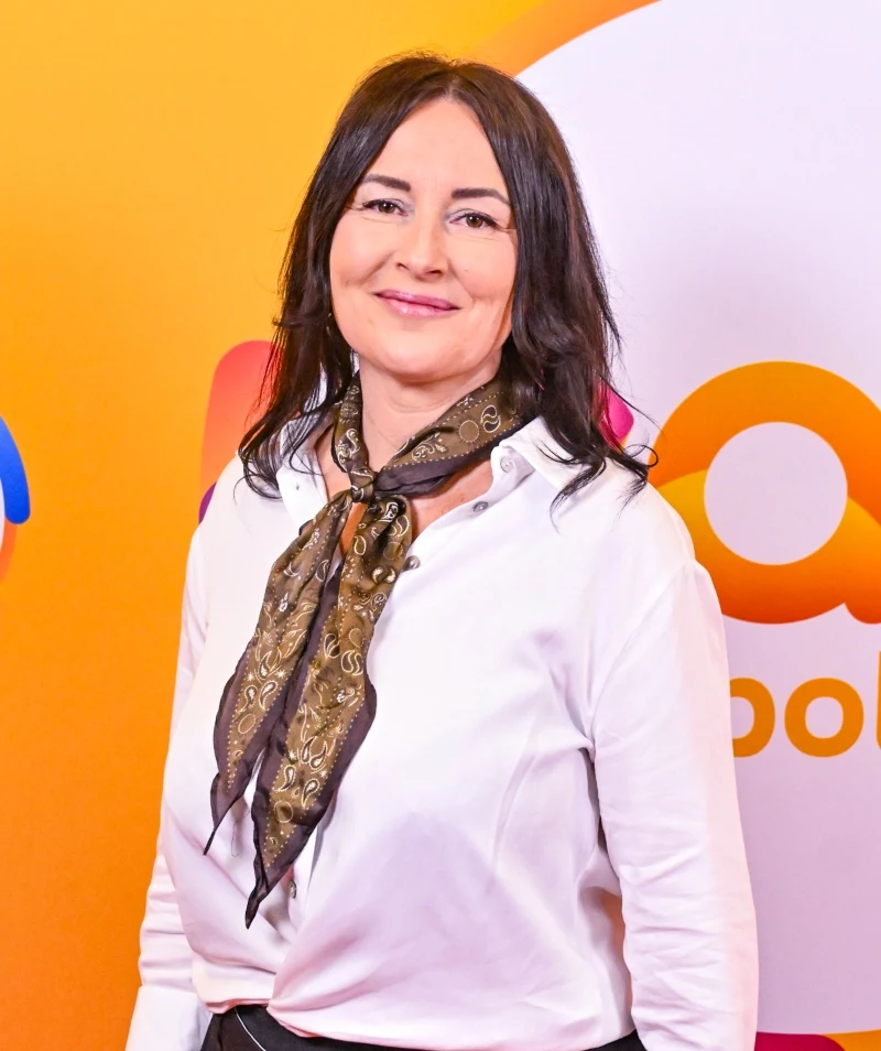 Emilia Kostrzewska podczas wizyty w "halo tu polsat" postawiła na apaszkę w kolorze czekolady. Dodatek zastąpił biżuterię do jasnej koszuli Kobieta z ciemnymi włosami, ubrana w białą koszulę i zdobiony apaszkę, stoi na tle kolorowej, graficznej ścianki z logo.