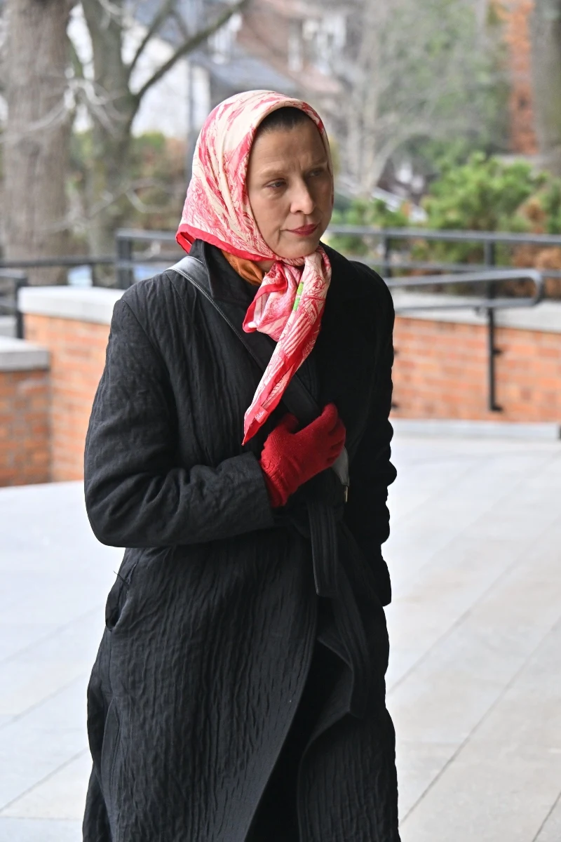 Katarzyna Herman chustę nosi również na głowie. Zestawiona z rękawiczkami prezentuje się rewelacyjnie. Kobieta w czarnym płaszczu, czerwonych rękawiczkach i różowej chustce na głowie idąca chodnikiem obok ceglanego muru.