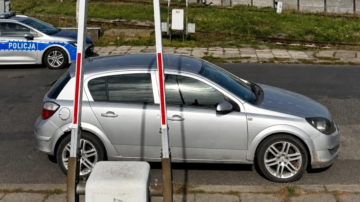 31-letnia kobieta zaparkowała samochód pod rogatkami przy przejeździe kolejowym srebrny opel zaparkowany pod rogatkami przejazdu kolejowego, widoczny policyjny radiowóz w tle