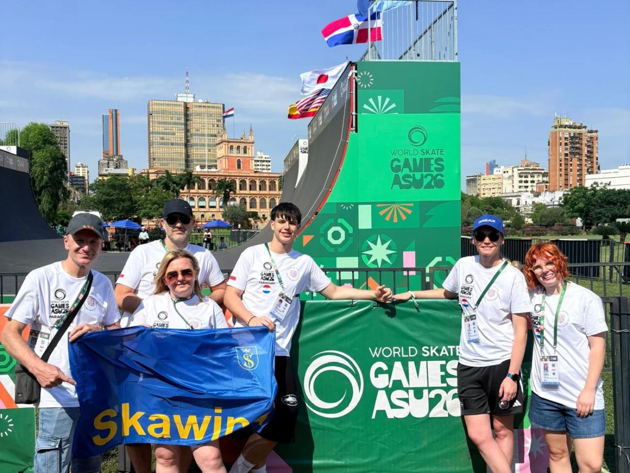 Skawińska reprezentacja podczas World Skate Games ASU26 w Paragwaju Grupa sześciu osób pozuje przed rampą i banerem World Skate Games ASU 2026, trzymając flagę z napisem Skawina.