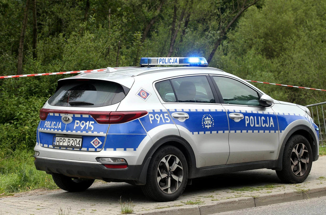 Policjanci udaremnili ucieczkę nietrzeźwej z miejsca zdarzenia. Zdj. ilustracyjne. Radiowóz polskiej policji z włączonymi sygnałami świetlnymi, zaparkowany obok taśmy odgradzającej teren.