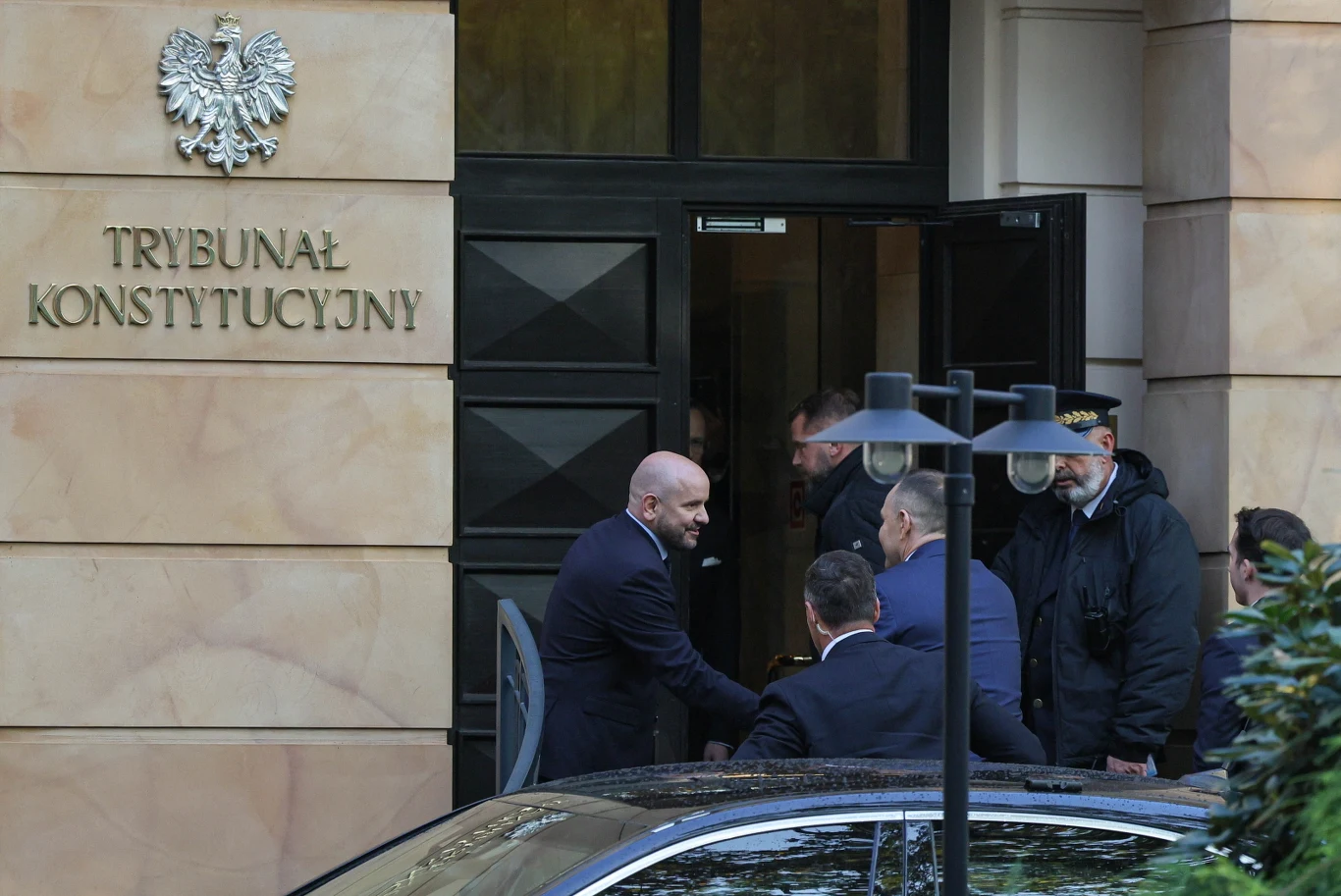 grupa mężczyzn w garniturach wchodzi do budynku trybunału konstytucyjnego, jeden z nich podaje rękę drugiemu przy wejściu