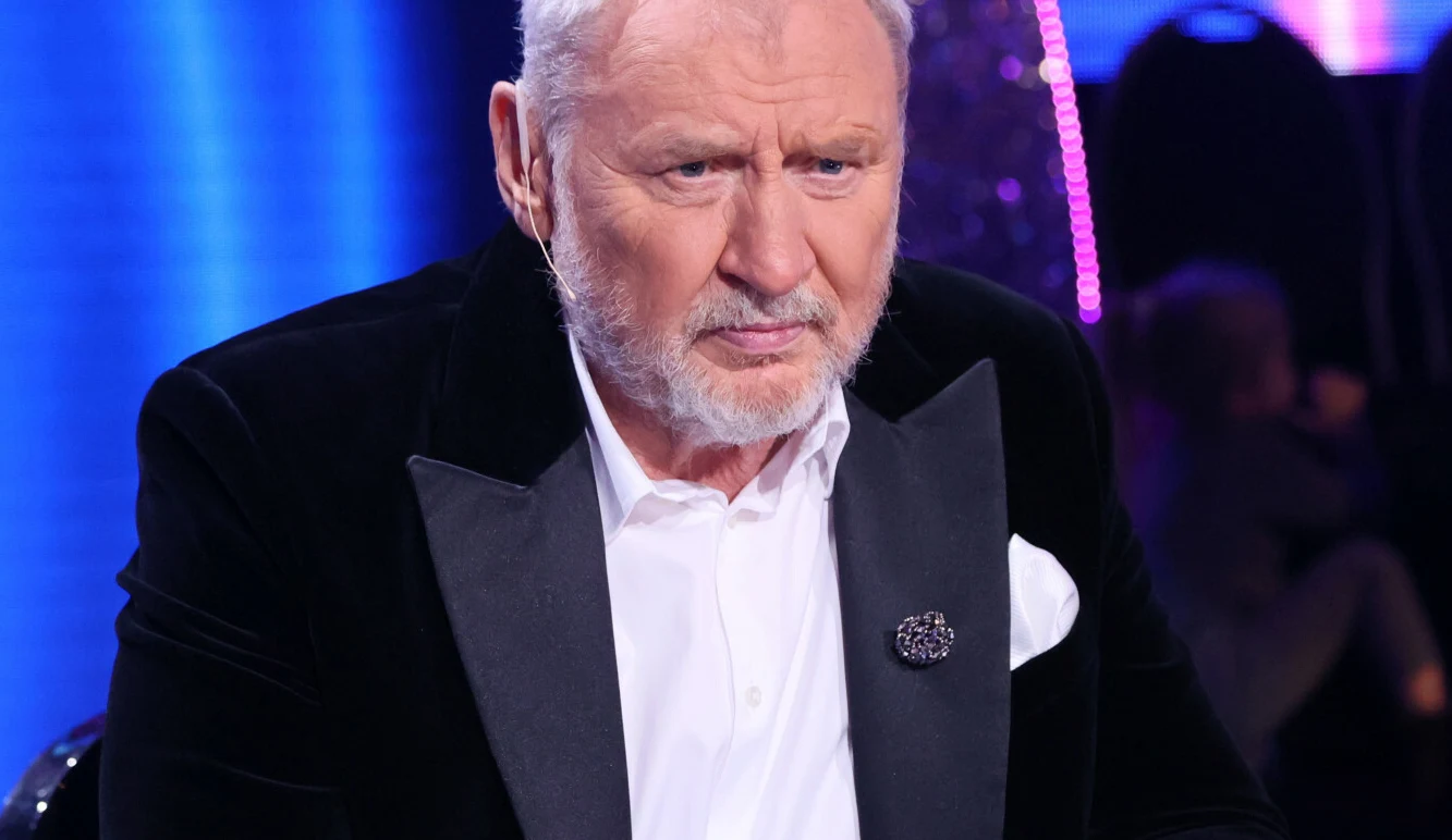 Andrzej Grabowski Andrzej Grabowski w eleganckim smokingu siedzi przy stole w jasnym studio.