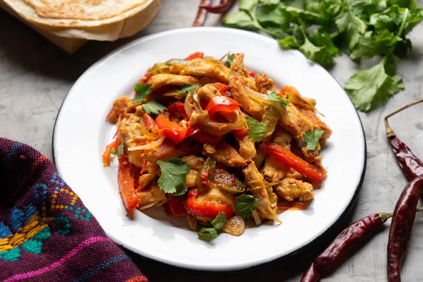 Fajitas z kurczaka to idealny obiad na weekend lub w środku tygodnia. Wystarczy 20 minut Fajitas z kurczaka z czerwoną papryką i świeżą kolendrą na talerzu, z tortillą i chili w tle