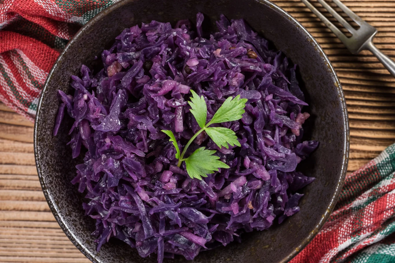 Rotkohl - pyszna dodatek do obiadu z czerwonej kapusty. Pasuje do schabowego i roladek duszona czerwona kapusta rotkohl z natką pietruszki w ciemnej misce na drewnianym stole