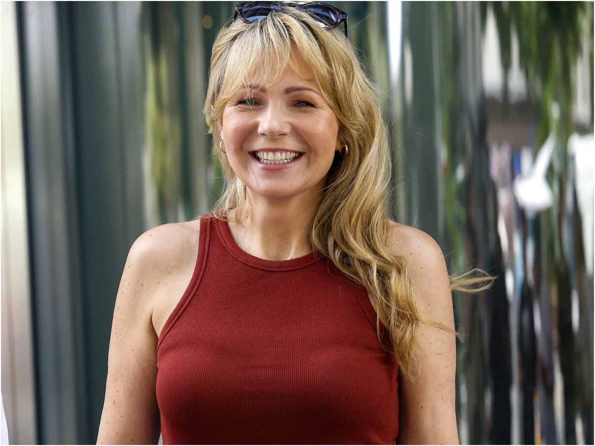 Anna Guzik Anna Guzik uśmiechnięta w czerwonej bluzce bez rękawów, z blond włosami i okularami przeciwsłonecznymi na głowie.