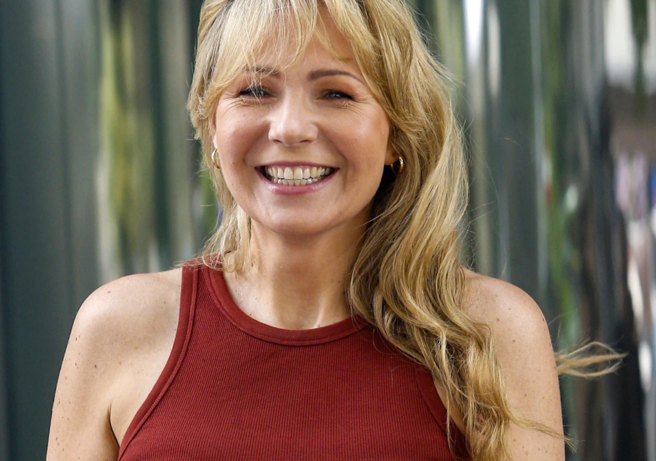 Anna Guzik Aktorka Anna Guzik z długimi blond włosami, ubrana w czerwony bezrękawnik, uśmiecha się do obiektywu.