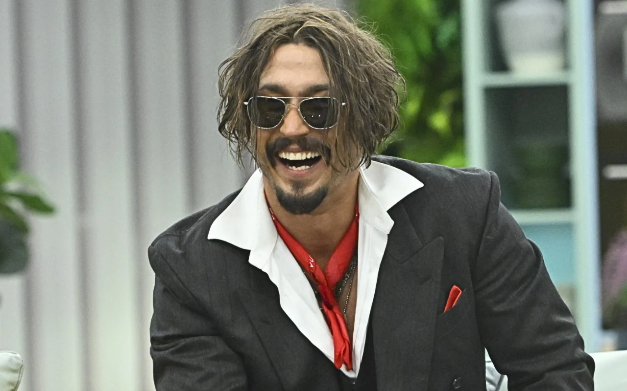 Tihon Shevtsov, sobowtór Johnny'ego Deppa. Mężczyzna w ciemnych okularach i rozczochranych włosach, ubrany w czarną marynarkę, biały kołnierzyk i czerwony apaszkę, śmieje się szeroko, siedząc w jasnym, nowoczesnym wnętrzu.