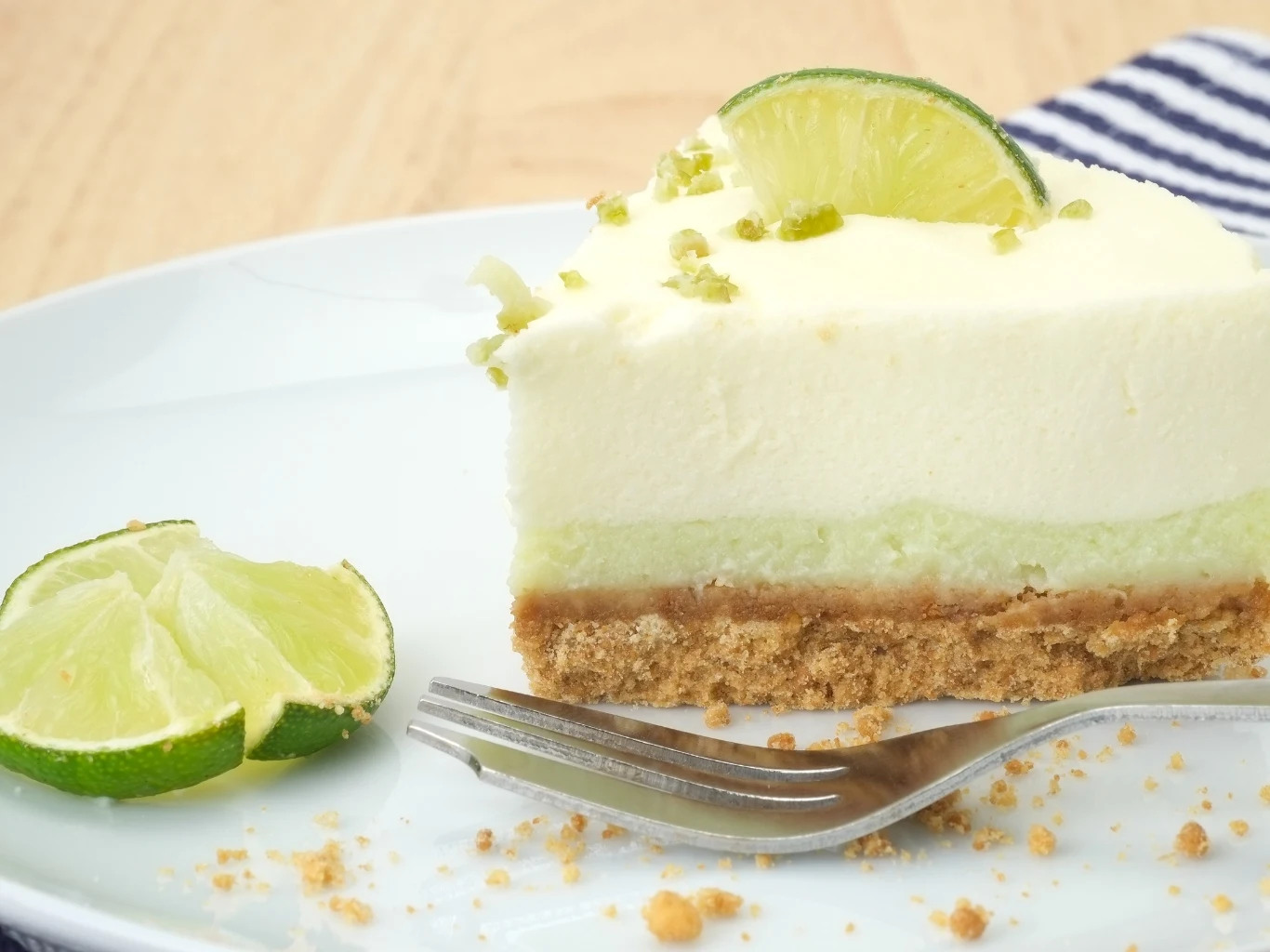 Sernik na zimno z sokiem z limonki. Sernik na zimno z jasnozieloną limonkową warstwą na spodzie z herbatników, z plasterkiem i skórką limonki.