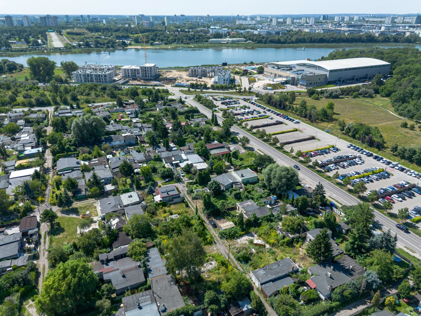 Osiedle Maltańskie w Poznaniu, 13 sierpnia 2026 rok osiedle domków jednorodzinnych otoczone zielenią, sąsiadujące z dużym parkingiem i nowoczesnym kompleksem sportowym nad brzegiem rzeki