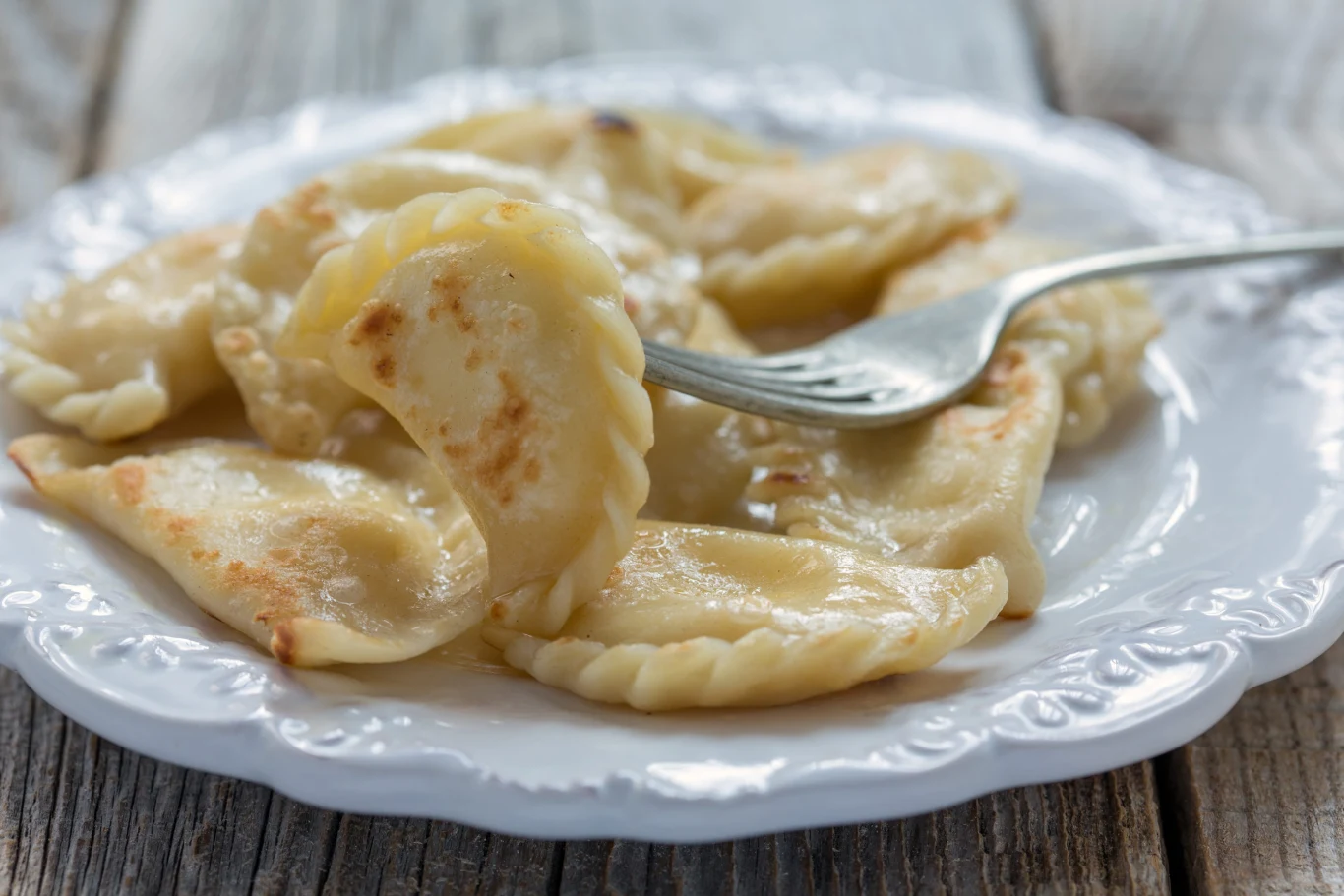 Przed podaniem rumienię je na roztopionym maśle Pierogi z serem podsmażone na maśle, podane na białym talerzu, jedna porcja na widelcu
