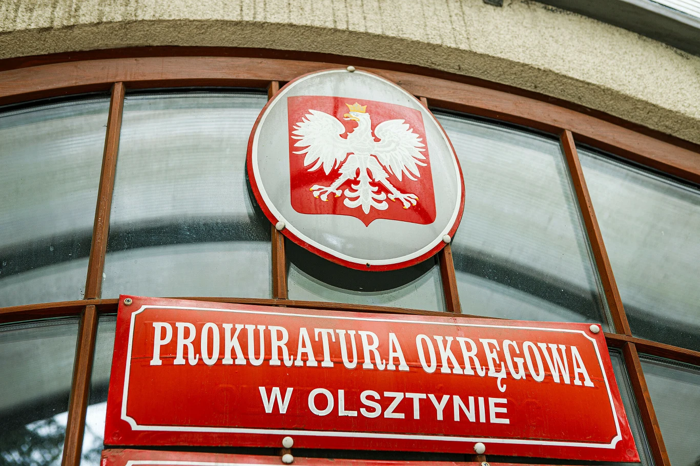 Prokuratura Okręgowa w Olsztynie. Zdj. ilustracyjne Tablica z napisem 'Prokuratura Okręgowa w Olsztynie' i godło Polski na tle przeszklonej fasady.