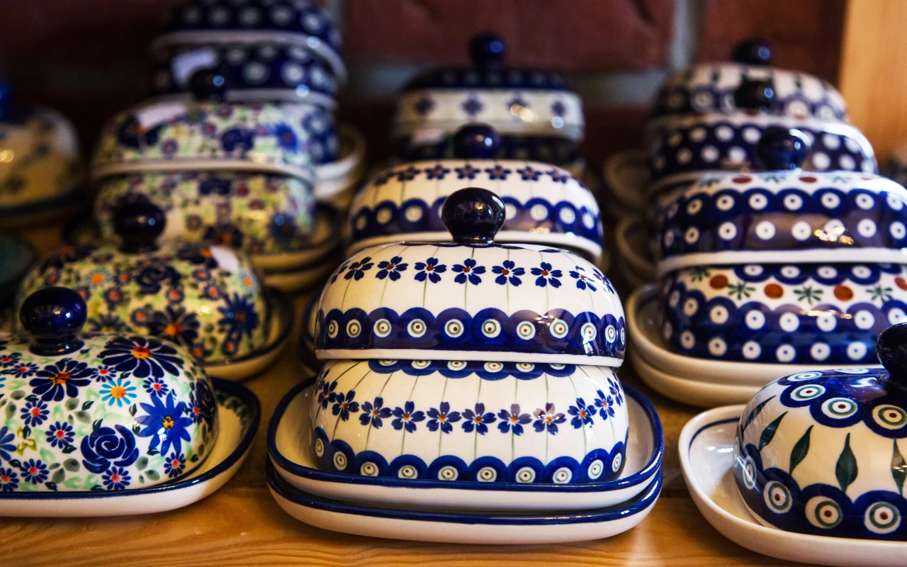 Bolesławiecka ceramika zachwyca w Korei Rząd ceramicznych maselnic zdobionych tradycyjnymi wzorami w niebieskich i białych barwach, ustawionych na drewnianej półce.