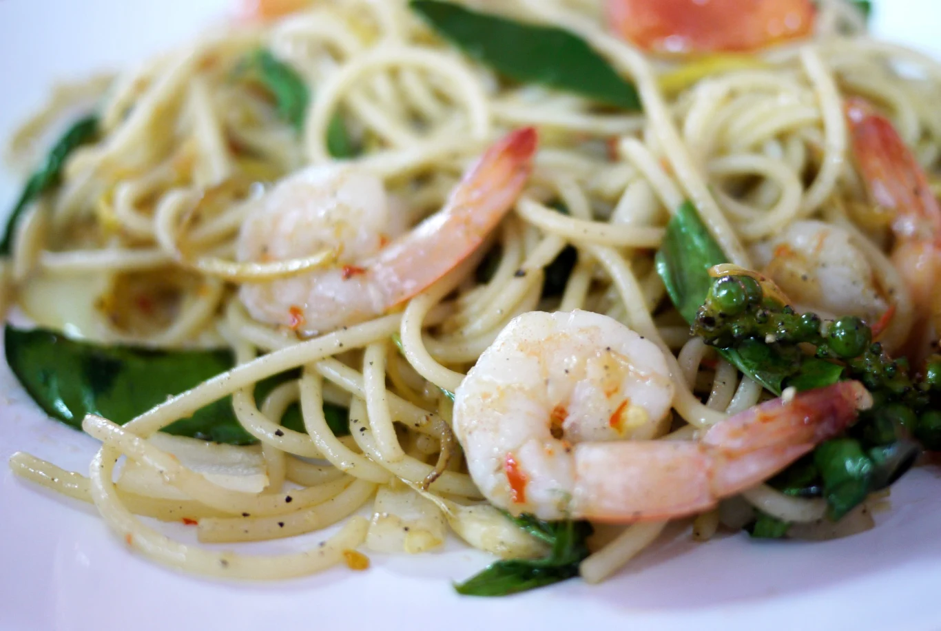 Krewetki, szpinak, czosnek i pomidorki to zestaw idealny Makaron spaghetti z krewetkami, szpinakiem i pomidorkami na białym talerzu