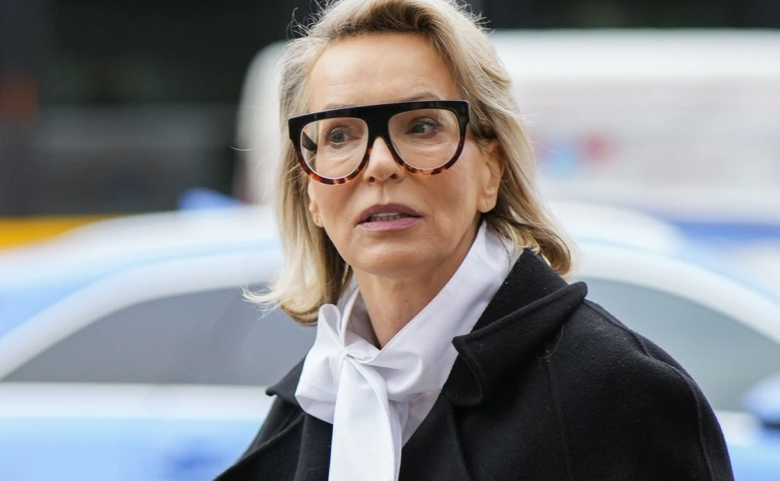 Paulina Smaszcz Paulina Smaszcz w okularach i białej bluzce z kokardą, na tle przestrzeni miejskiej.
