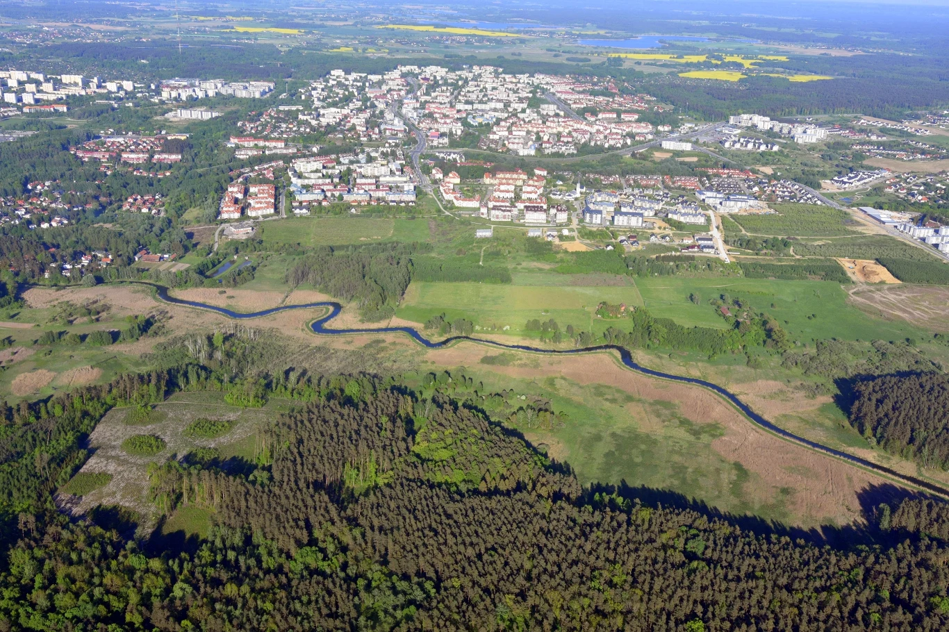 Olsztyn przejmie tereny sąsiednich gmin? Radni szykują oficjalną propozycję. Panorama Olsztyna z zabudową mieszkalną i osiedlami, oddzielona od lasu rzeką i pasem zielonych łąk