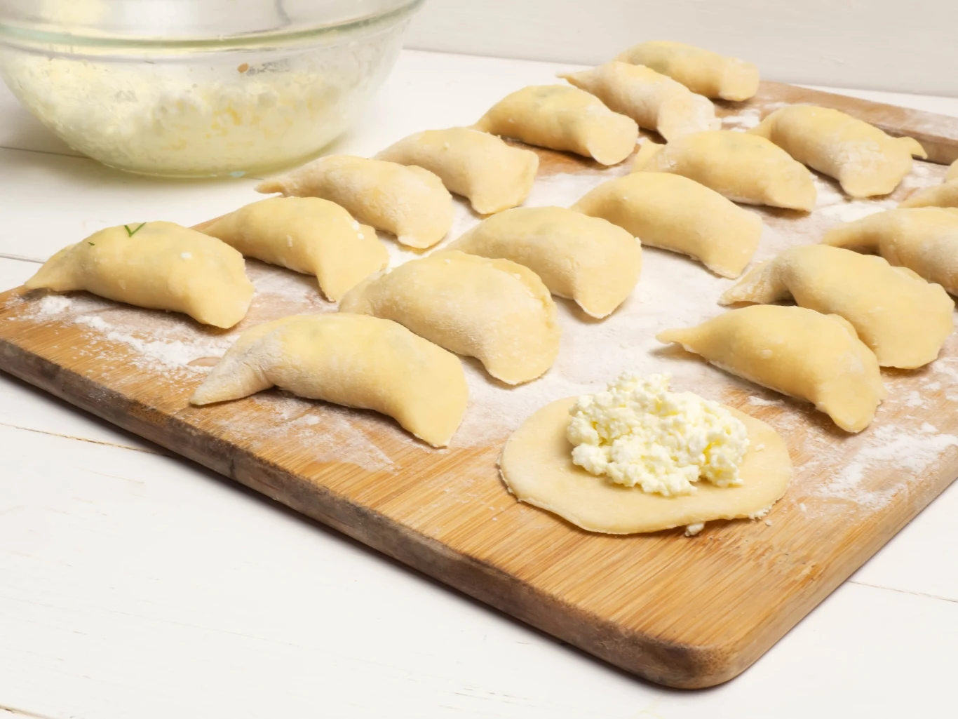 Moje ciasto na pierogi jest miękkie i sprężyste. Olej zastępuje innym tłuszczem. Surowe pierogi z farszem na drewnianej desce oraz miska z nadzieniem przygotowane z ciasta na bazie masła.