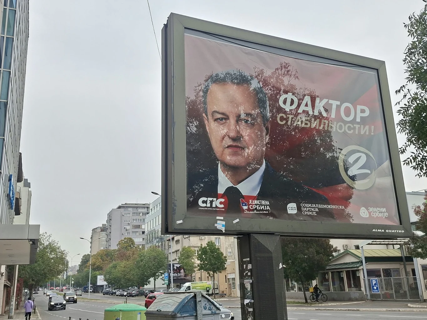 Szef MSW i jego wyborczy plakat Duży billboard z portretem mężczyzny w garniturze, hasłem wyborczym w języku rosyjskim oraz logotypami partii politycznych, ustawiony przy ulicy w otoczeniu budynków i samochodów.