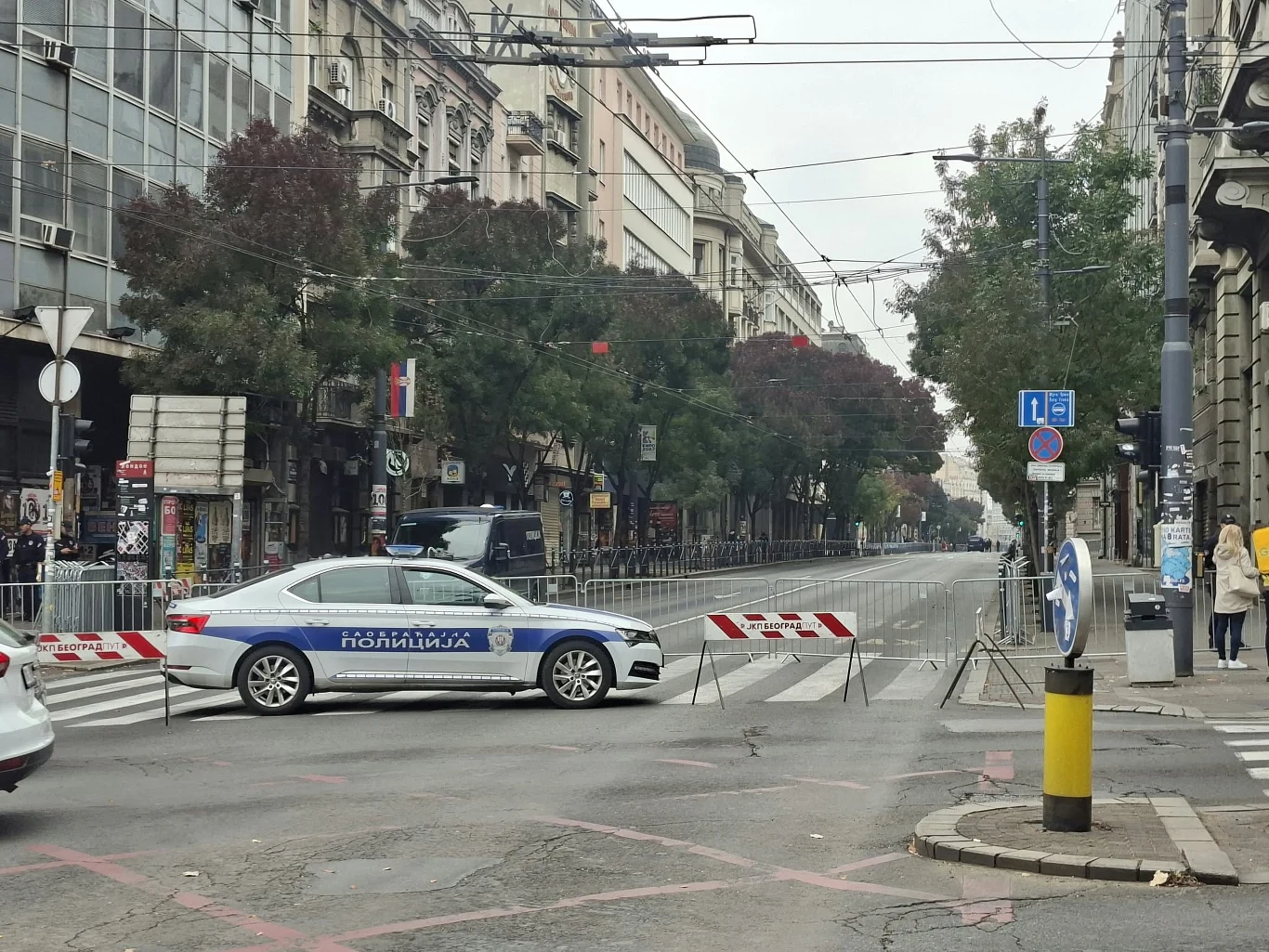 Okolice siedziby prezydenta Serbii strzeżone przez mundurowych w dniu wyborów do Zgromadzenia Narodowego Radiowóz policyjny blokujący pustą ulicę w centrum miasta, otoczony barierkami zabezpieczającymi przejazd.