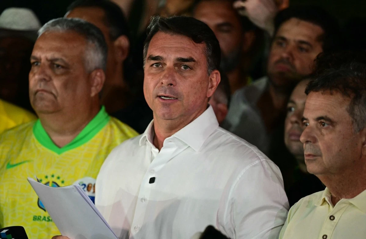 Flavio Bolsonaro po ogłoszeniu pierwszych wyników drugiej tury wyborów prezydenckich w Brazylii Mężczyzna w białej koszuli stoi na pierwszym planie, trzymając dokumenty, otoczony przez grupę ludzi uważnie słuchających jego wystąpienia.