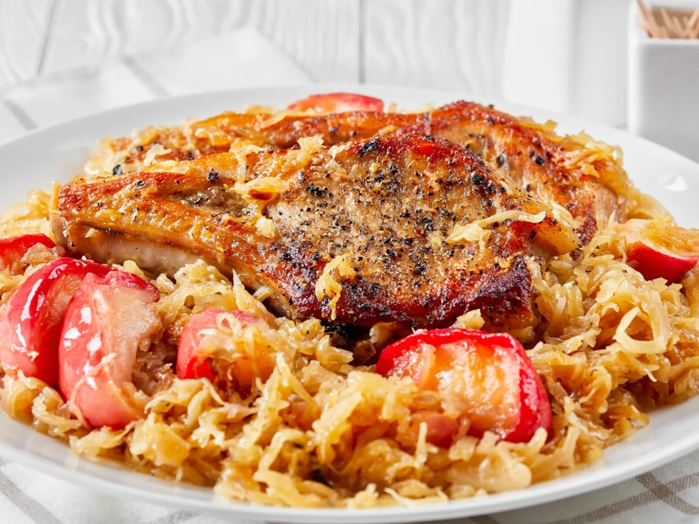 Pieczone kotlety schabowe w kapuście będą idealne na obiad na Wszystkich Świętych. Pieczone kotlety schabowe podane na kapuście z kawałkami czerwonych jabłek w naczyniu żaroodpornym