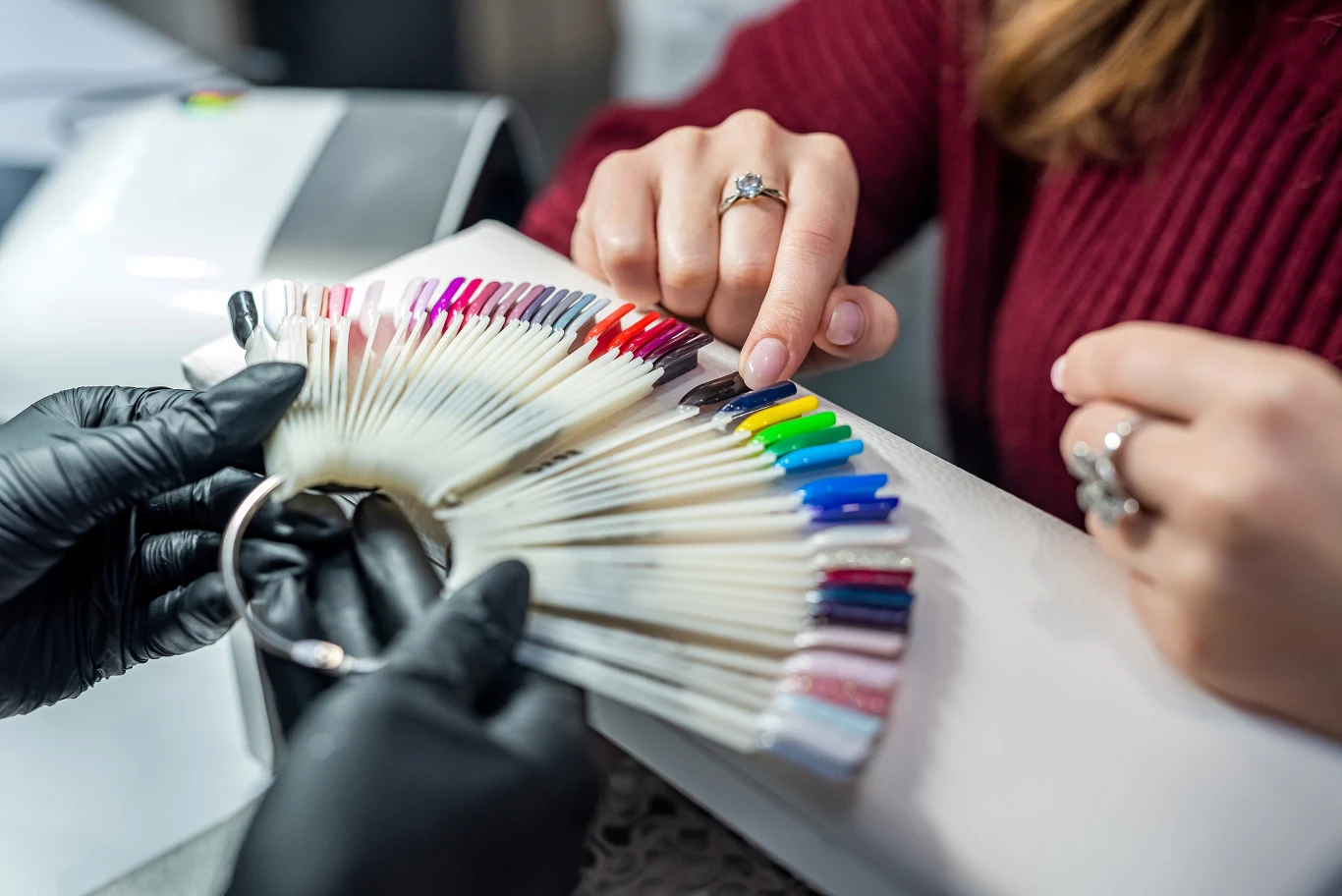 Na jaki manicure postawić jesienią? Próbnik lakierów do paznokci w jesiennej kolorystyce trzymany przez stylistkę w czarnych rękawiczkach.