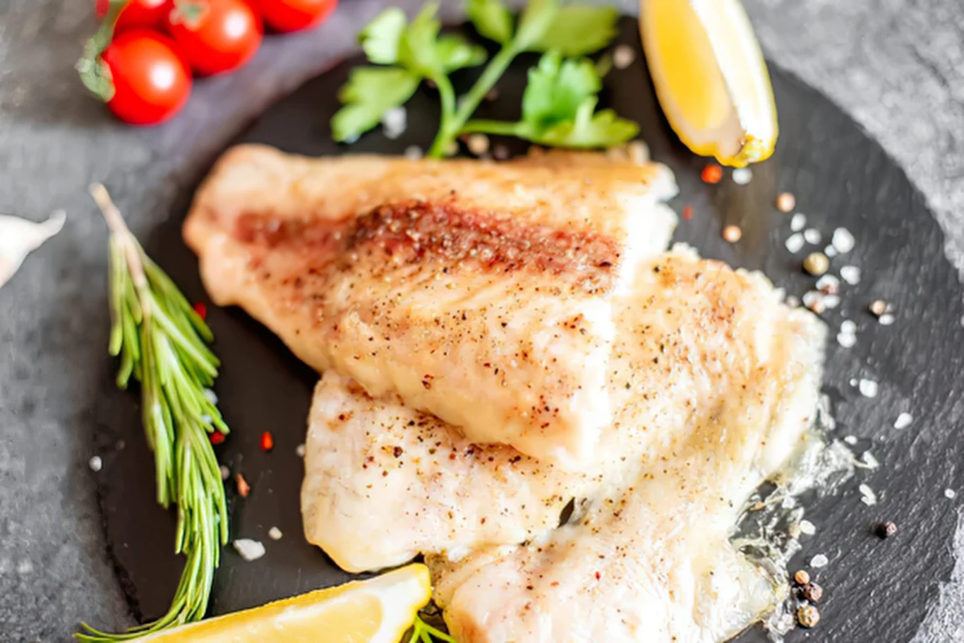 Polska smaczna ryba, lepsza od karpia i dorsza. Szkoda, że zapomniana. Pieczony filet z suma podany z cytryną, świeżymi ziołami i pomidorkami koktajlowymi na talerzu.