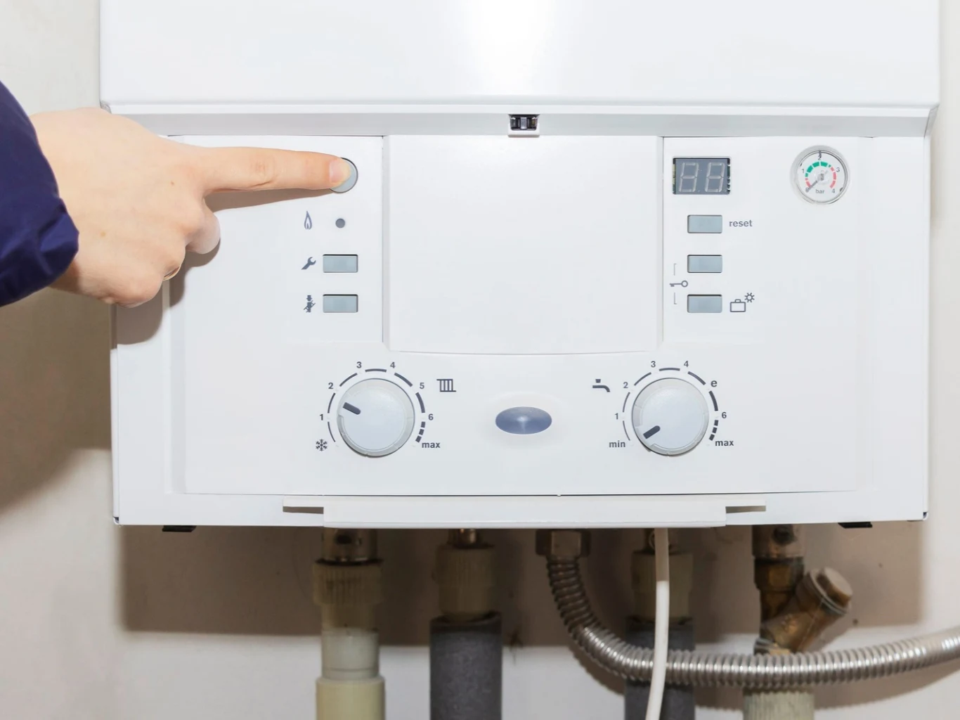 Panel sterowania kotła gazowego z widocznymi pokrętłami regulacyjnymi, elektronicznym wyświetlaczem, manometrem i ręką naciskającą przycisk.