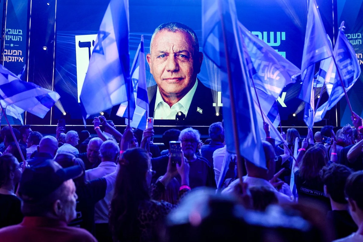 Gadi Eisenkot to główny kandydat do pokonania premiera Binjamina Netanjahu Tłum ludzi z izraelskimi flagami zgromadzony przed dużym ekranem wyświetlającym portret mężczyzny na tle niebieskich świateł i banerów wyborczych.