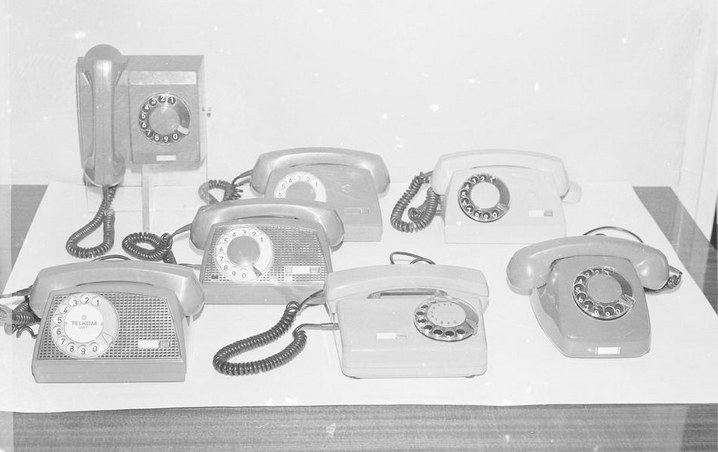 Aparaty telefoniczne. W pierwszym szeregu od lewej: Storczyk, Tulipan, Jaskier. W drugim szeregu Storczyk. W trzecim szeregu od prawej dwa aparaty Aster. Z tyłu jedyny wiszący aparat Irys (1976) /Z archiwum Narodowego Archiwum Cyfrowego