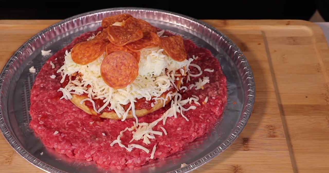 Baza w formie mrożonej pizzy, ogromny kawał mięsa z minipizzą, która za chwilę zostanie przykryta kolejną warstwą mięsa /YouTube